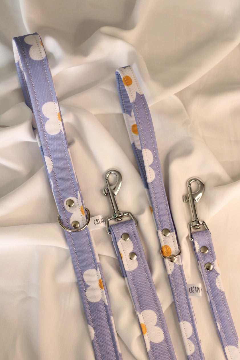 Two purple dog leashes with white flower patterns on a light fabric background